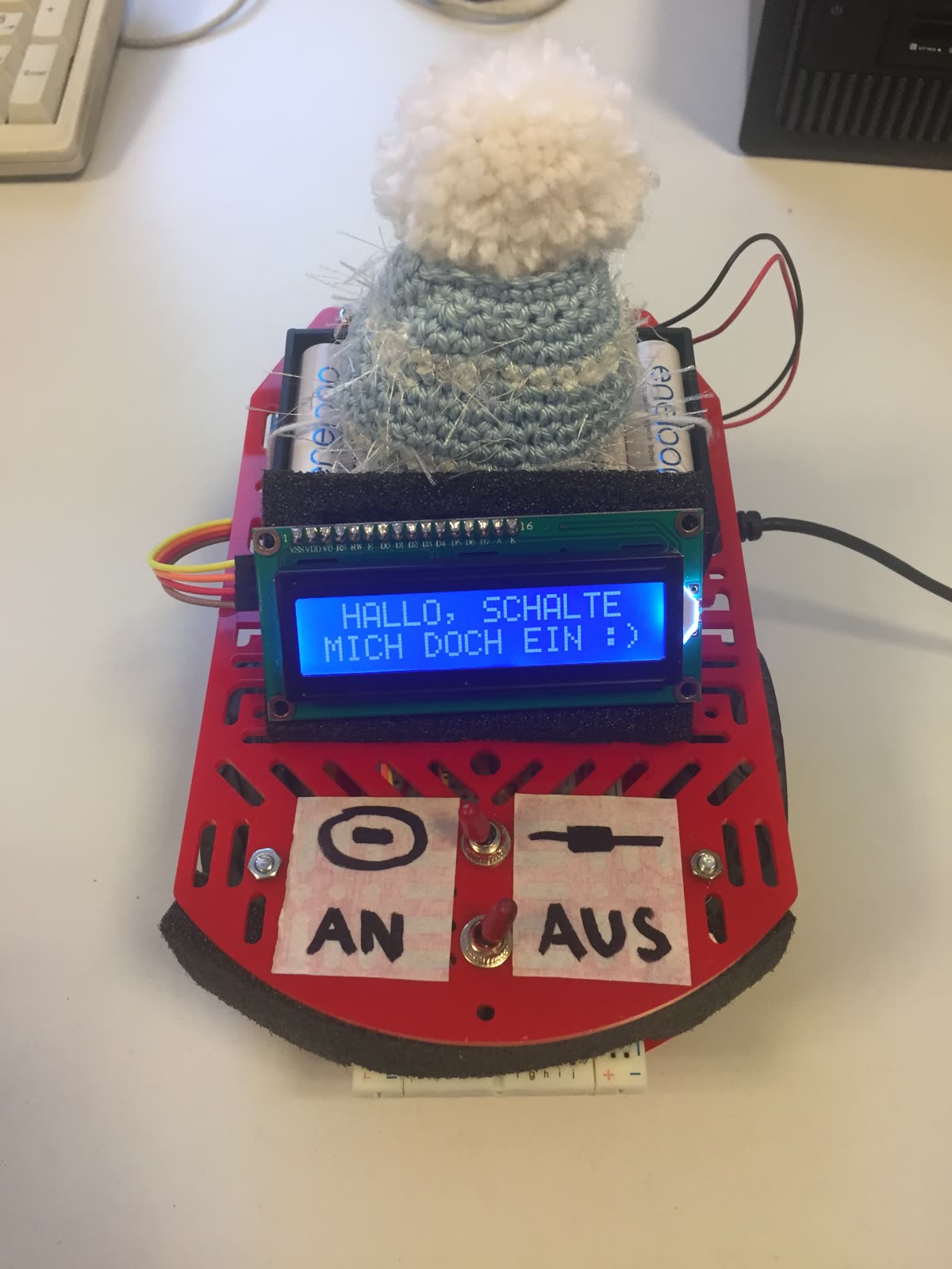 Rotes Fahrzeug mit Strickmütze und Display „Hallo, schalte mich doch ein :)“ sowie An- und Aus-Schild