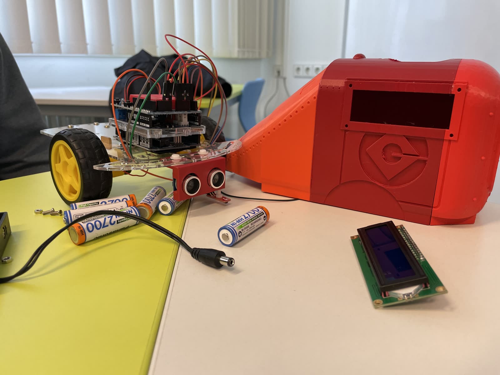 Fahrzeug mit Arduino und großem rotem, 3D-gedrucktem Gehäuse, daneben Akkus und ein Display