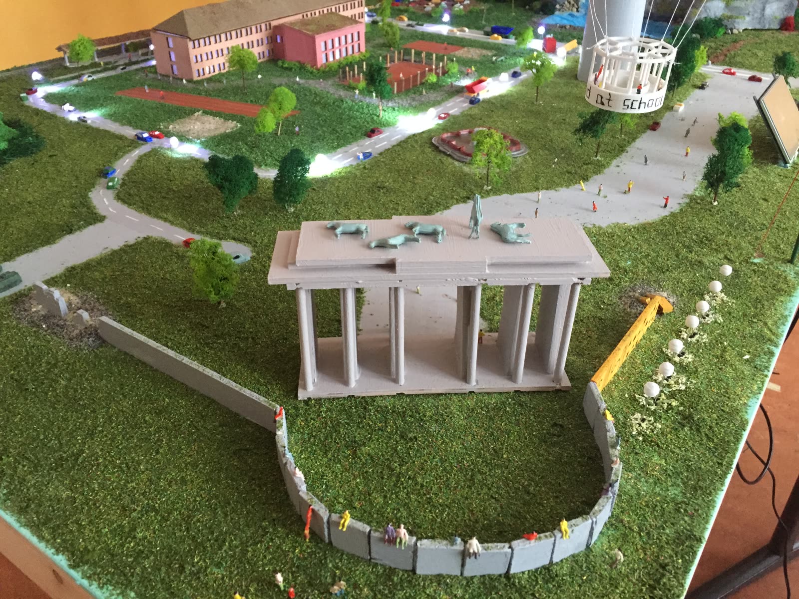 3D-gedrucktes Brandenburger Tor mit Mauerstück auf einer Grünfläche, im Hintergrund ein Heißluftballon