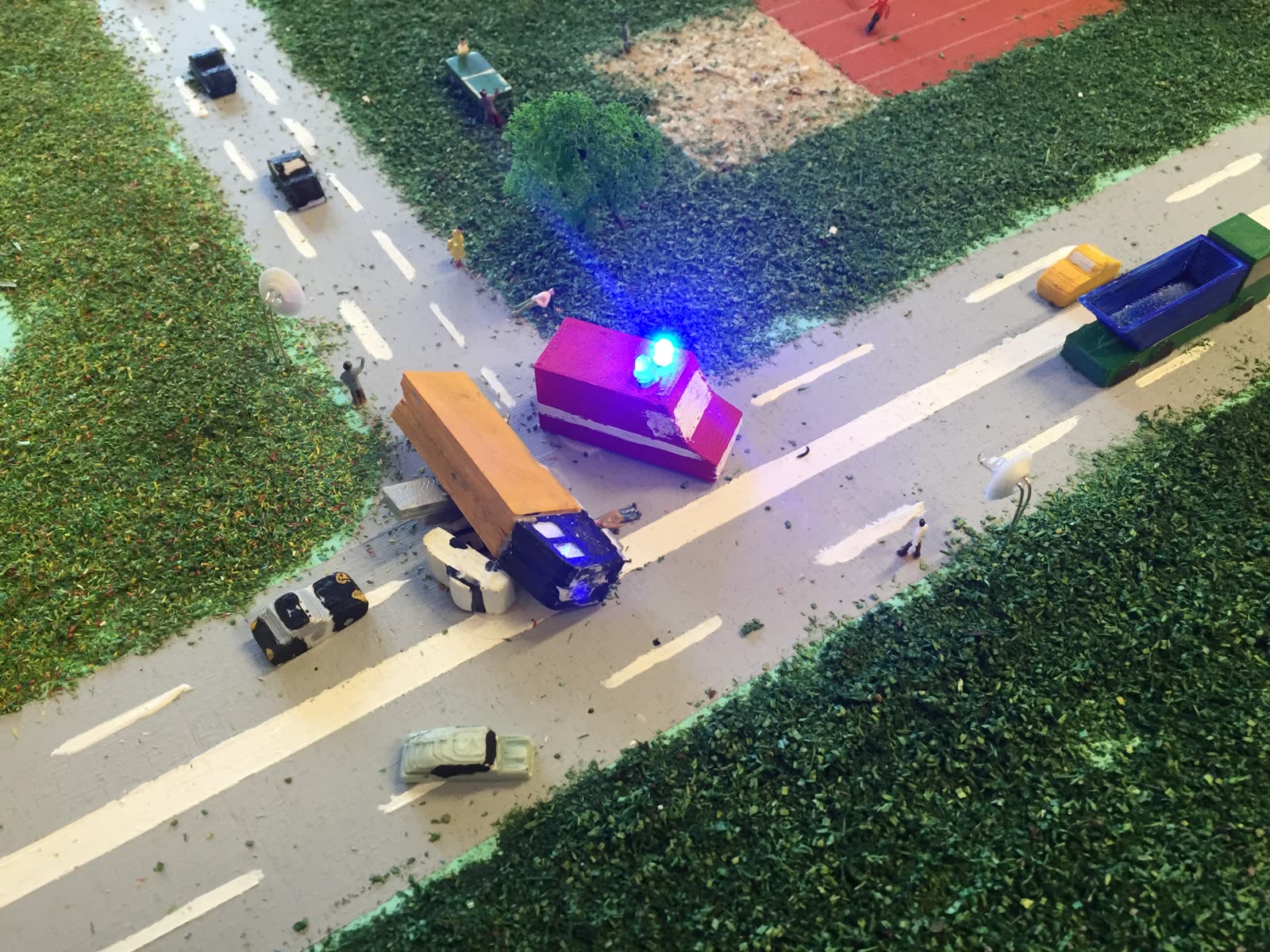 Unfallszene auf einer Modellstraße mit Polizei- und Rettungswagen mit blauem Blaulicht