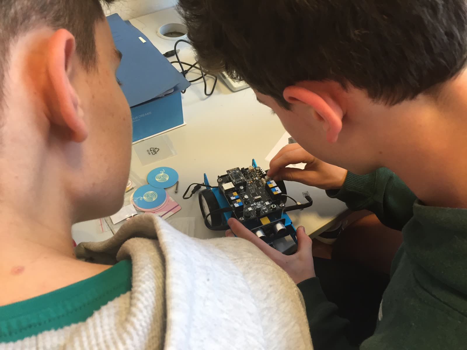 Zwei Schüler beugen sich über einen mBot und stecken Kabel an der Platine ein