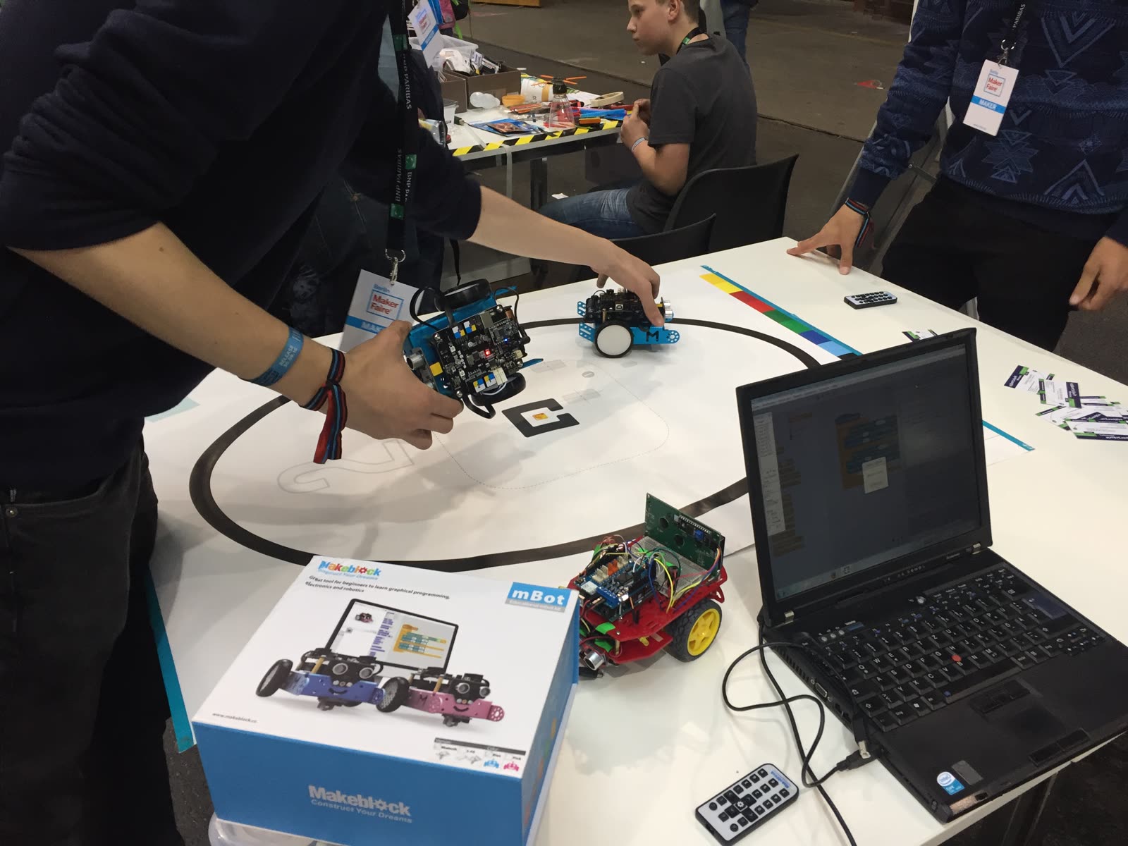 Ausstellungstisch mit mehreren mBots, einem Laptop und einer Rundstrecke, Besucher probieren die Roboter aus