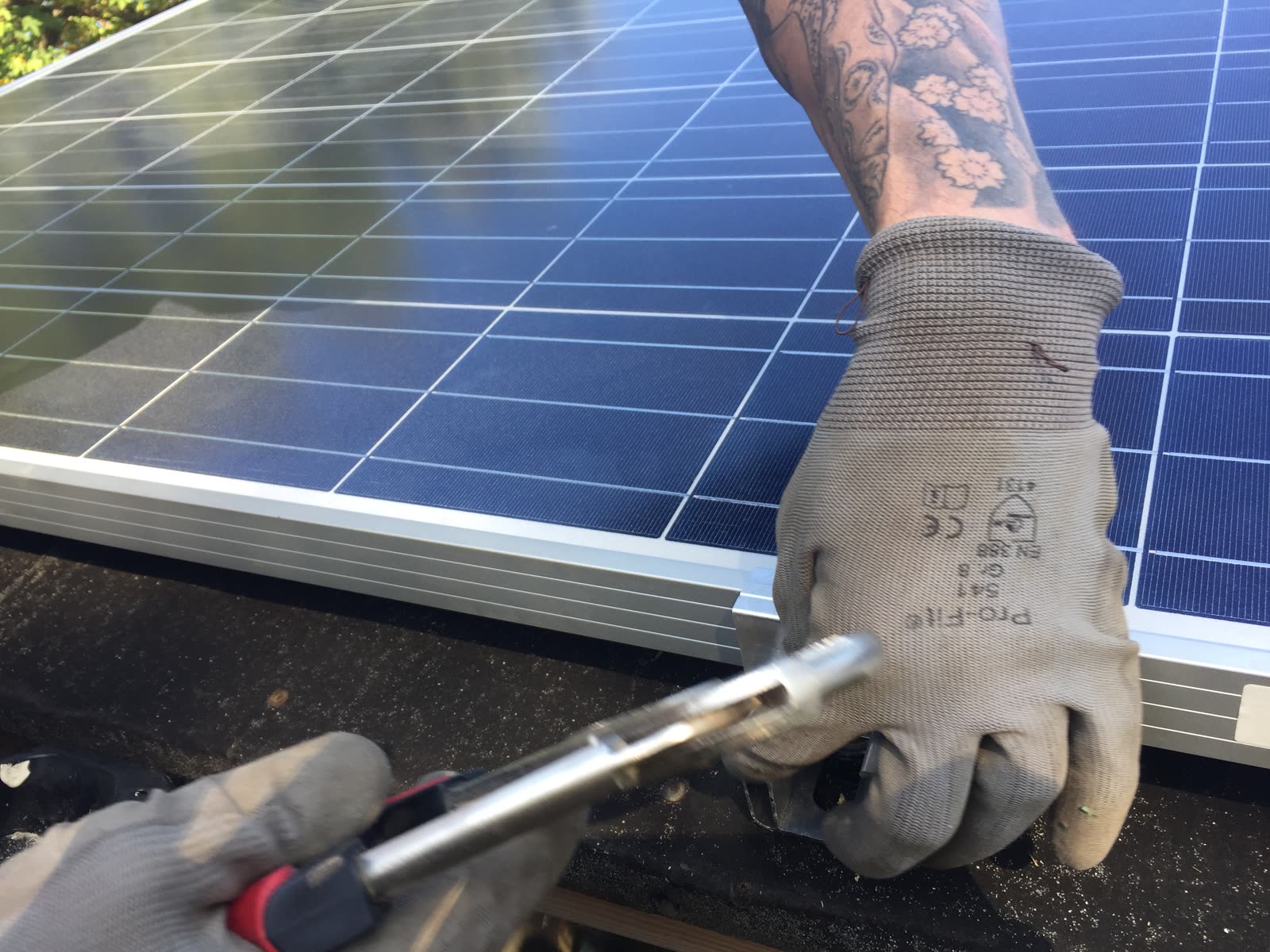 Hände in Arbeitshandschuhen befestigen den Rahmen eines Solarmoduls mit einer Zange