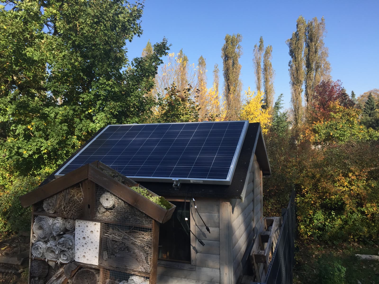 Fertig montiertes Solarmodul auf dem Dach des Gartenhäuschens vor herbstlichen Bäumen