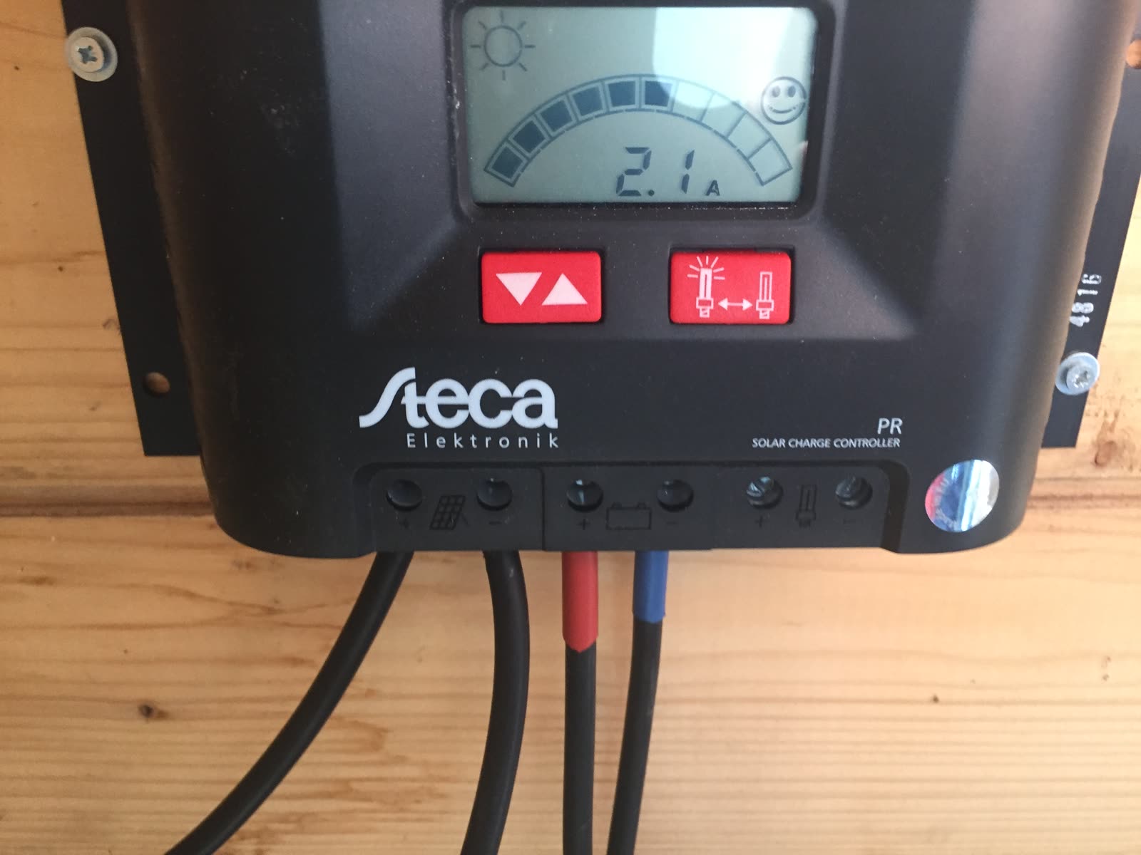 Solar-Laderegler mit Display und angeschlossenen roten und schwarzen Kabeln an einer Holzwand