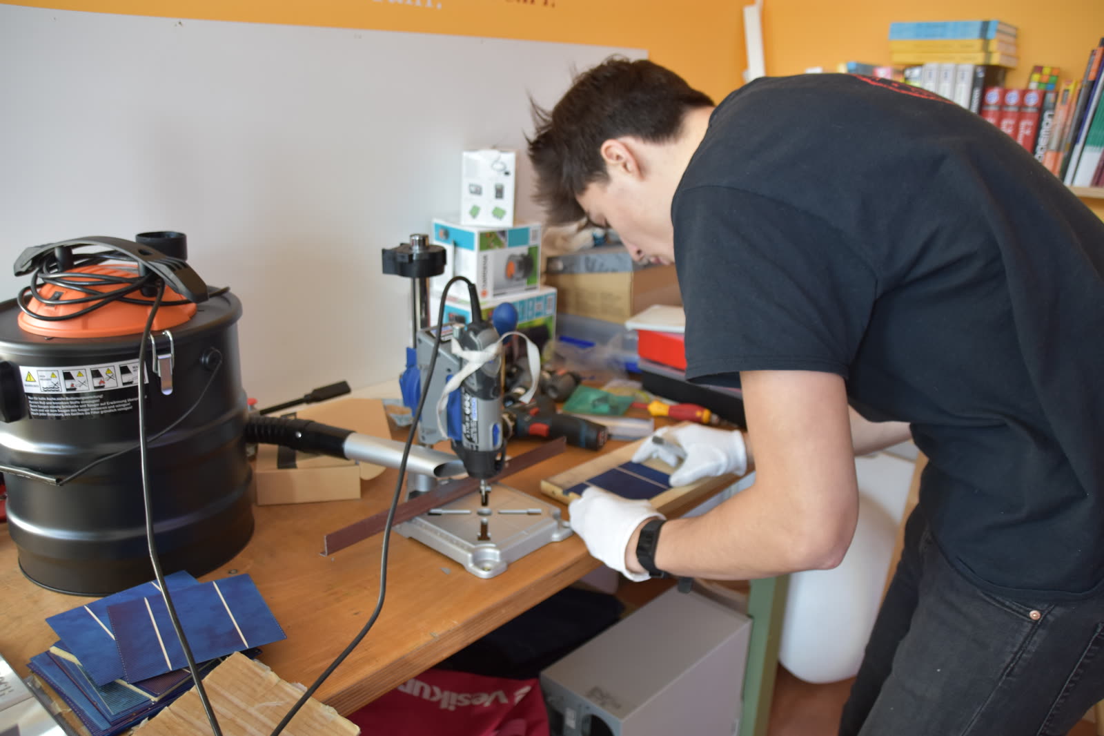 Schüler mit Schutzhandschuhen bearbeitet Solarzellen an einer Werkbank mit Bohrständer