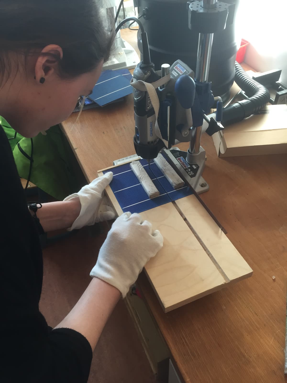 Hände in weißen Handschuhen legen Solarzellen in eine selbst gebaute Holzlehre