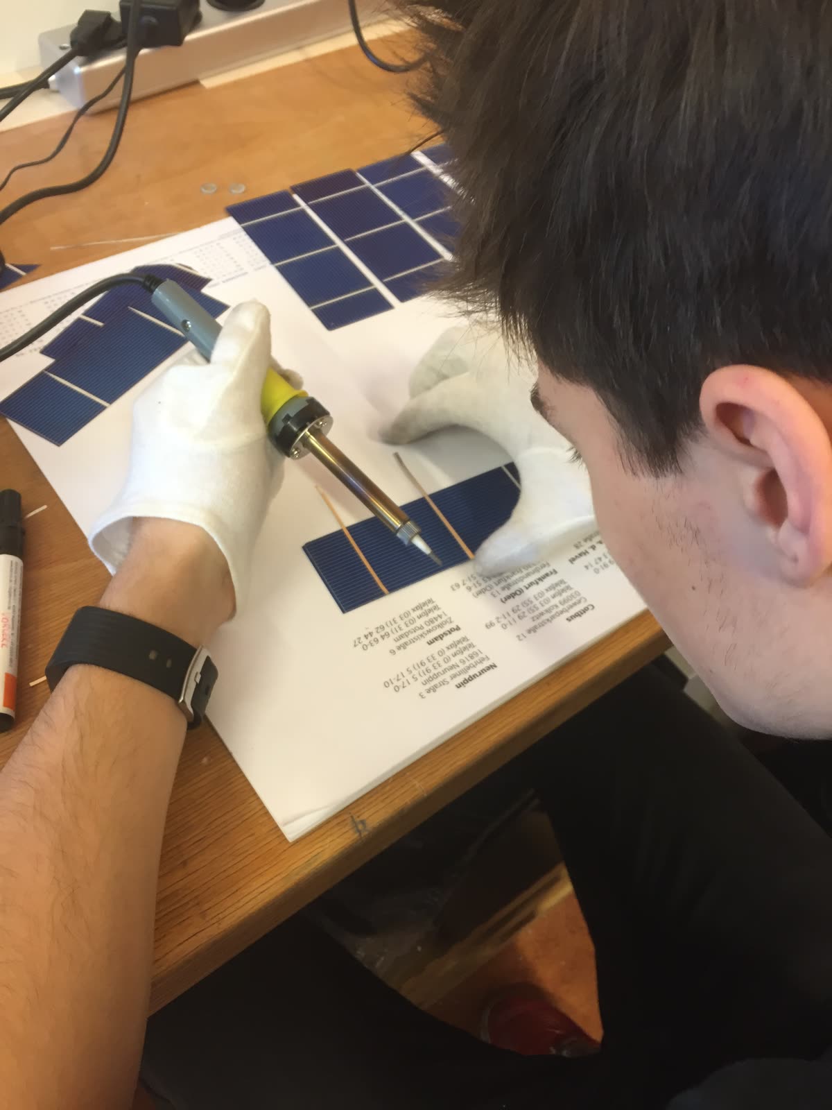 Schüler lötet mit einem Lötkolben Verbinder auf eine Solarzelle