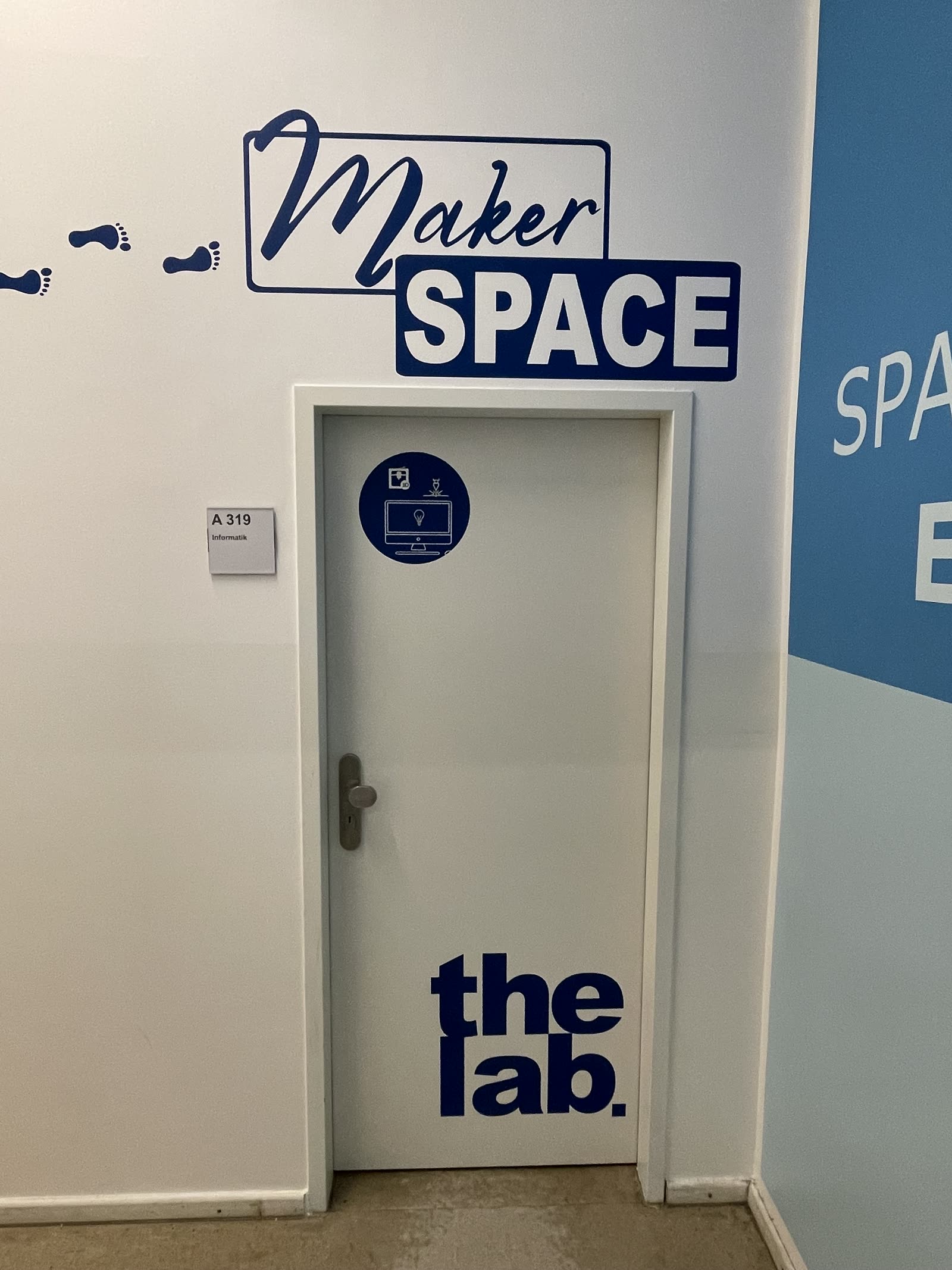 Tür mit dem Schriftzug „Maker Space“ darüber und „the lab“ auf der Tür, dazu Fußspuren an der Wand