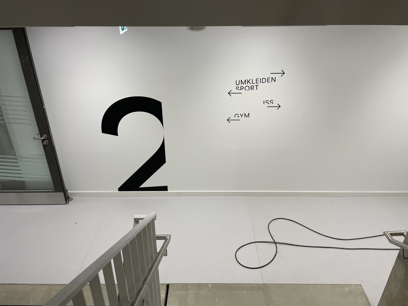 Große Ziffer 2 mit Wegweisern zu Umkleiden, Sport und Gym an einer Treppenhauswand